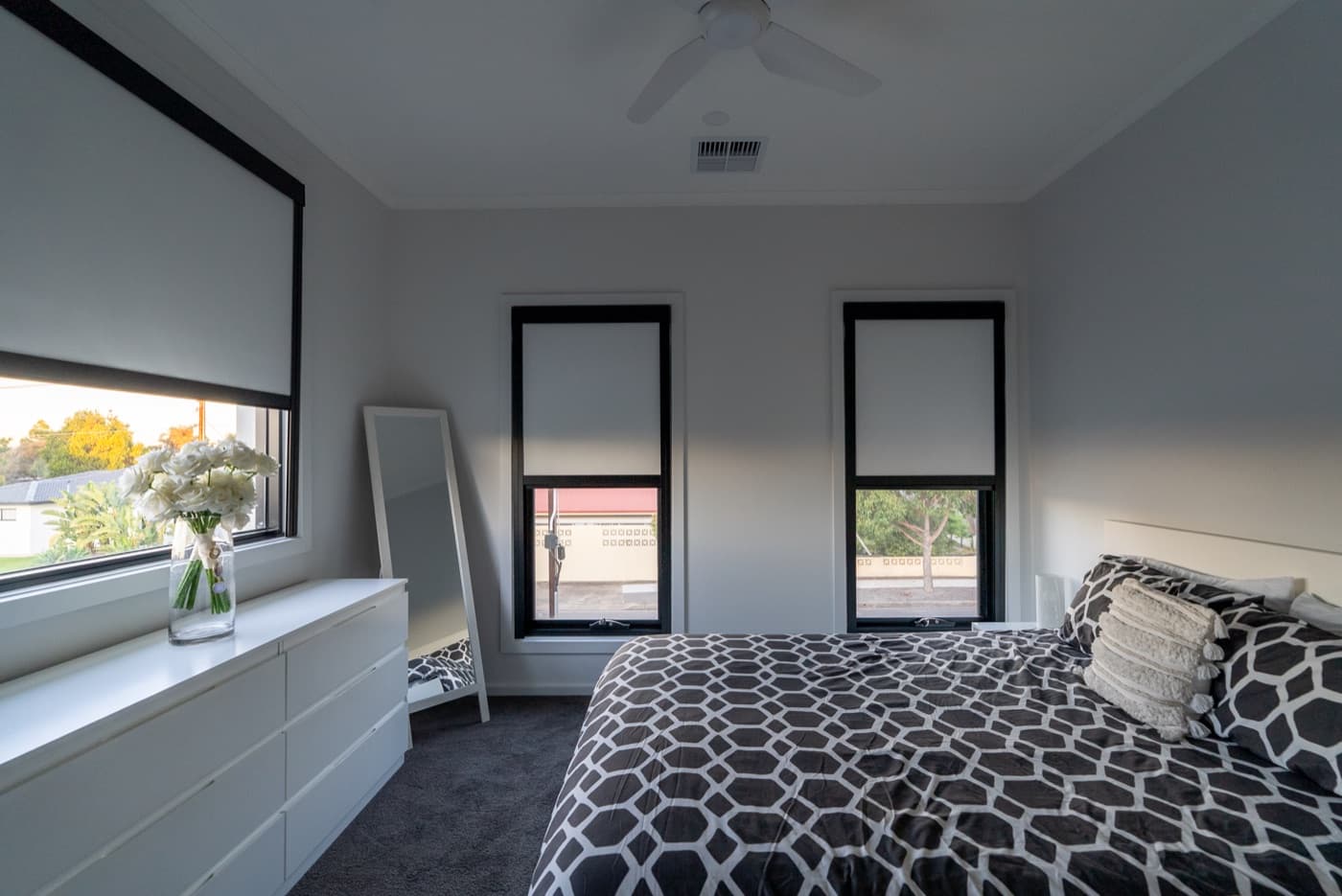 Black-frame motorised blackout blinds part-lowered across three bedroom windows.