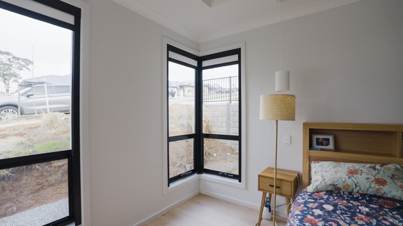 Black-frame corner windows in a bedroom with a blackout blind.