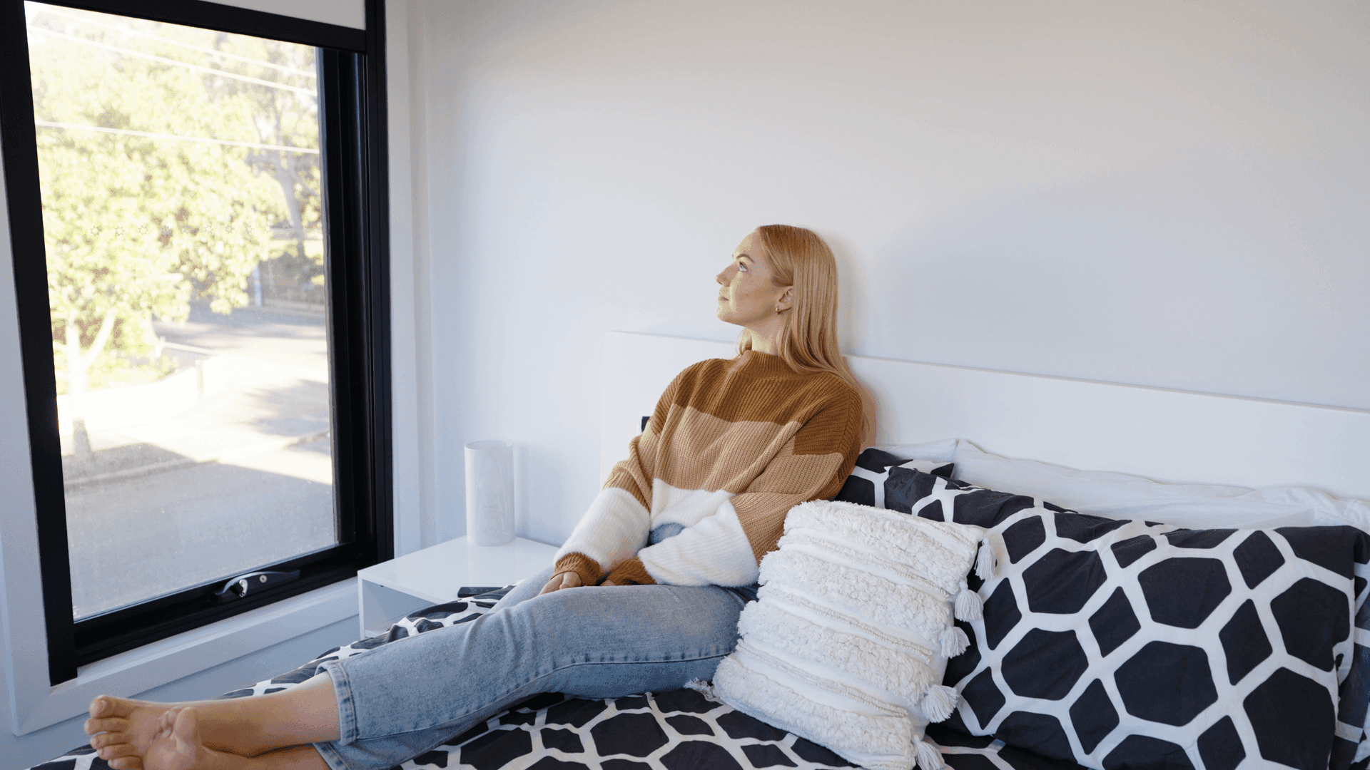 Customer relaxing on a bed beside a black-frame blackout blind.