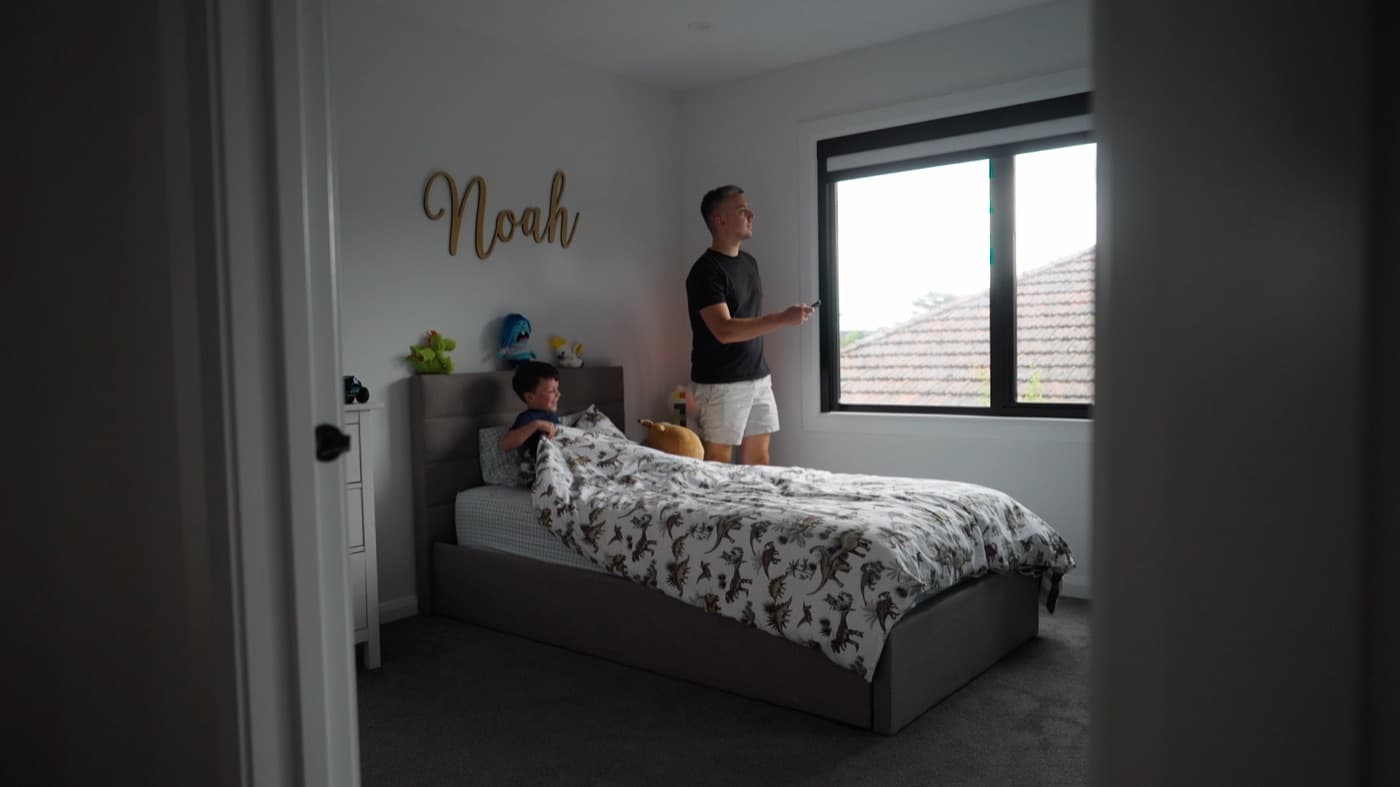 Customer using the remote to close a motorised blackout blind in a bedroom.