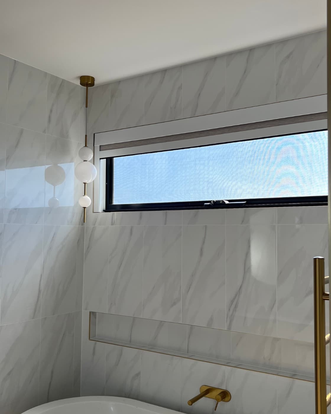 Marble-tiled bathroom with a dark-frame blackout blind fitted to the high window.
