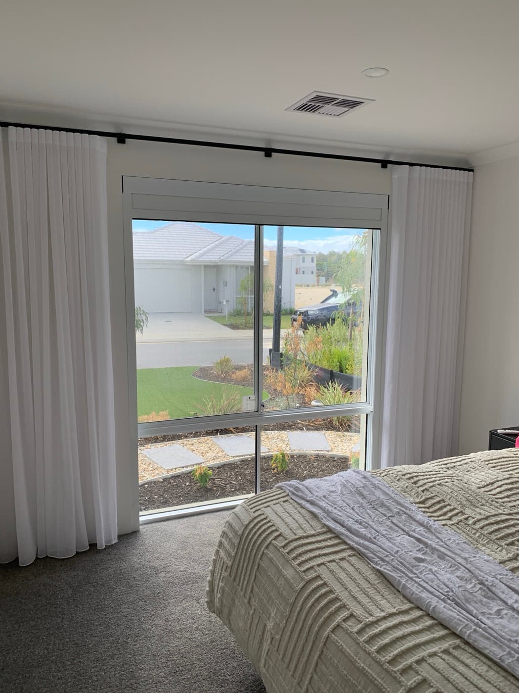 White-frame blackout blind in a bright bedroom with sheer curtains.