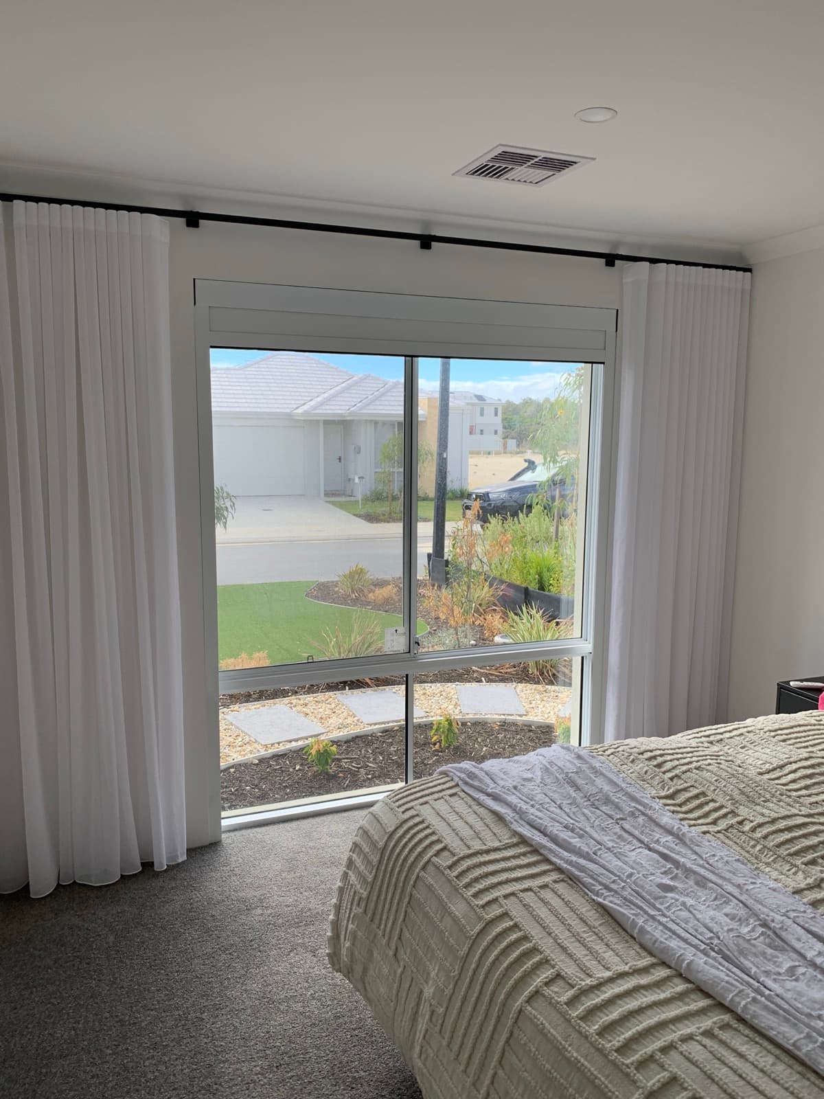 Apartment bedroom with a white-frame blackout system over a glass door and a suburban outlook.